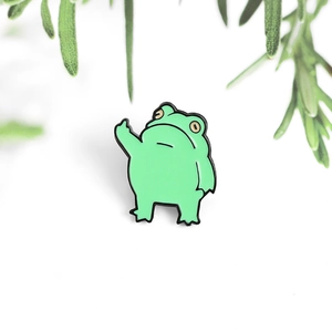 Détail d'un pin's grenouille rigolo en émail vert faisant un doigt d'honneur sur fond blanc