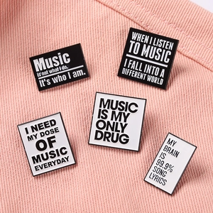 Close-up of five black and white music-themed enamel pins on pink fabric background