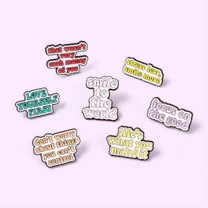 Flat lay of colorful enamel pins with inspirational quotes on a light purple background
