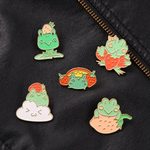 Set of five green frog enamel pins with strawberry and rainbow details on black leather