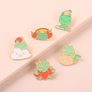 Close-up of five cute frog enamel pins with strawberry and rainbow details on pink backdrop
