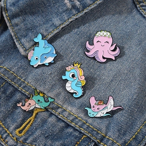 Detail of five cute ocean animal enamel pins on a denim jacket showing the vibrant colors