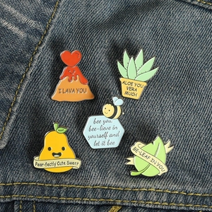 Detailed view of 5 cartoon enamel pins with bee and plant motifs on blue denim fabric