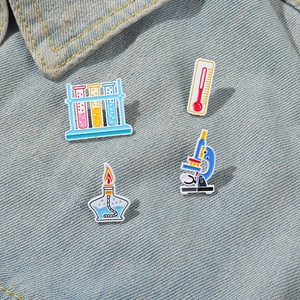 Set of four science-themed enamel pins featuring a microscope and test tubes on denim