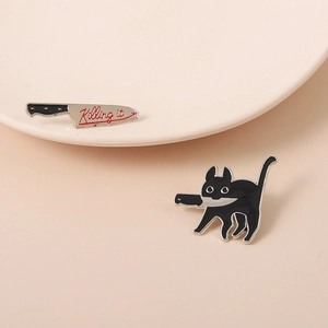 Detailed view of enamel pins featuring a black cartoon cat with a knife and Killing it text