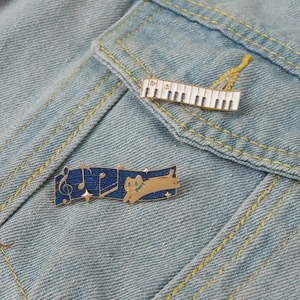 Cute enamel music pins featuring a piano keyboard and cat with notes on denim jacket