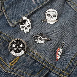 Close-up of gothic punk enamel pins featuring skull and moon cat designs on denim jacket