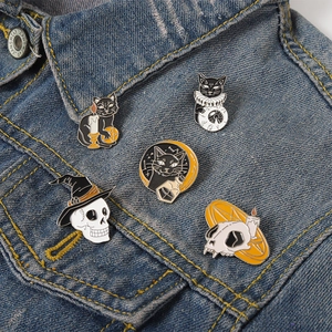 Detail shot of five dark gothic cat and skull enamel pins on blue denim fabric