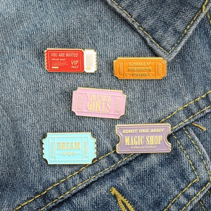 Close-up of five colorful ticket-shaped enamel pins on blue denim fabric background