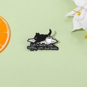 Détail d'un pin's émaillé avec chat noir, café et livres sur un fond vert pastel
