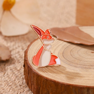 Broche en émail renard mignon en orange et blanc sur un plateau en bois rustique