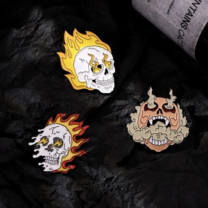 Three punk gothic flame skull enamel pins for clothing or bags on a dark background