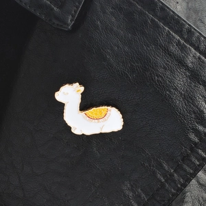 Close-up of a white alpaca enamel brooch with colorful saddle on black leather fabric