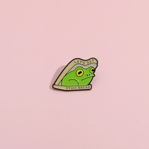 Detail of creative cartoon frog enamel pin featuring Let's Get This Bread slogan design