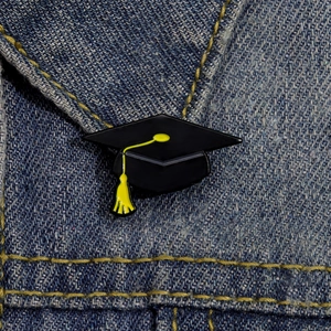 Detailed close-up of a graduation cap enamel pin on a blue denim jacket background