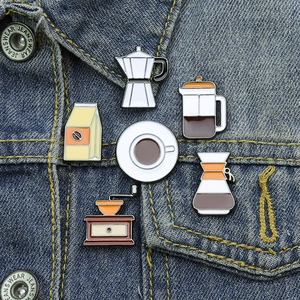 Close-up of six creative coffee-themed enamel pins displayed on blue denim fabric