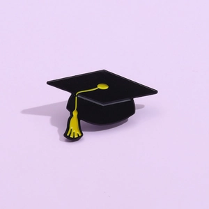 Macro shot of black enamel graduation cap brooch with yellow tassel on purple background