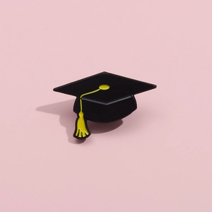 Detail of creative graduation cap enamel pin with yellow tassel on a pink surface