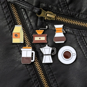 Detail of coffee theme enamel pins featuring a moka pot and grinder on a black leather jacket