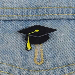 Classic black graduation cap enamel pin with yellow tassel on blue denim jacket