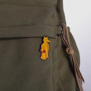 Close-up of a yellow enamel tapir pin on a green canvas backpack with leather drawstring