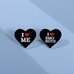 Detailed macro of two black heart enamel pins with I Love Me and I Love Emo Boys slogans