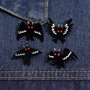 Detail of four black Mothman enamel pins with red eyes on blue denim background