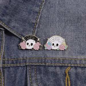 Artistic skull floral enamel pins with 'Til Death We Do Art' text on denim jacket
