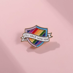 Detail of shield rainbow enamel pin with I'LL WALK WITH YOU text on a pink background