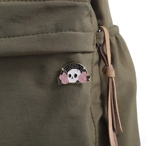 Detail of enamel skull and pink rose brooch pinned on a canvas bag with art slogan