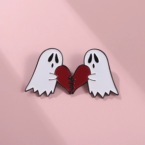 Detail of two-piece cartoon ghost enamel pins holding broken heart halves in white and red