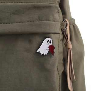 Close-up of a cartoon ghost enamel pin with heart on olive green canvas bag fabric