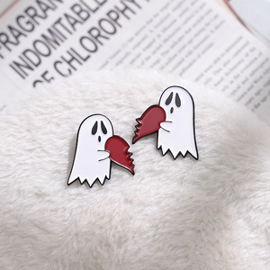 Close-up of matching cartoon ghost enamel pins holding two halves of a broken red heart