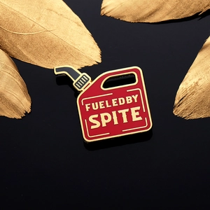 Red gas can enamel pin with 'FUELED BY SPITE' gold lettering on reflective black background