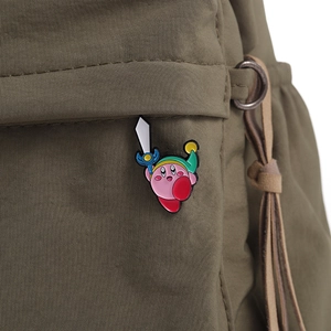 Close-up of pink Kirby enamel pin with sword on a green nylon backpack fabric