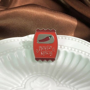 Gros plan d'un pin's en émail Neuro Spicy rouge en forme de sachet de chips sur porcelaine