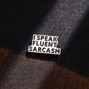 Detail of enamel pin with 'I SPEAK FLUENT SARCASM' text on a black textured backdrop