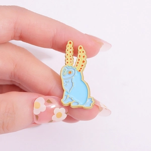 Creative blue rabbit enamel brooch with colorful ears held by hand on pink backdrop