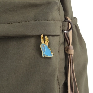 Blue rabbit enamel brooch with red dots pinned on a green canvas bag strap detail