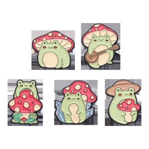 Set of five cute green frog and red mushroom enamel pins in creative cartoon designs