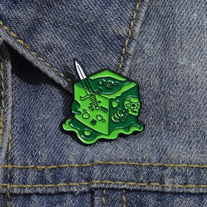 Close-up of a fantasy RPG skull and green liquid dagger enamel brooch on a denim jacket