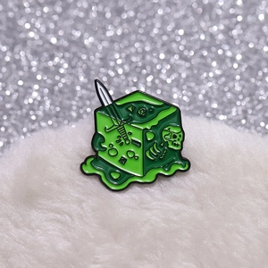 Macro shot of green liquid gelatinous cube enamel pin with skull and sword detail