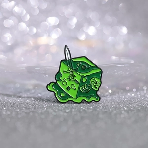 Macro detail of a green slime cube enamel pin with skull, sword and dice inside