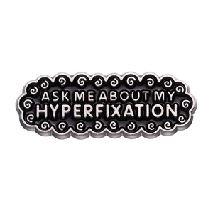 Οβάλ καρφίτσα σμάλτου με το κείμενο 'Ask me about my hyperfixation' σε μαύρο και ασημί