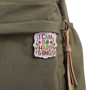 Enamel pin on a green canvas bag with 'I CAN DO HARD THINGS' text and floral pattern