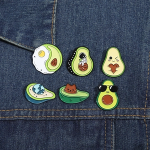 Detailed view of creative avocado enamel pins with cat and astronaut motifs on denim fabric