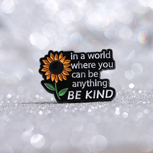 Close-up of 'Be Kind' enamel pin with sunflower detail and inspirational quote