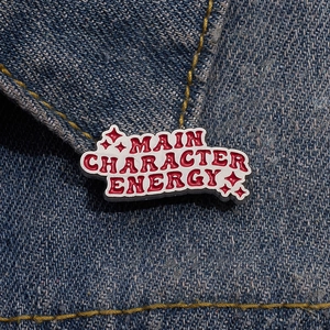 Enamel pin with 'Main Character Energy' text and red stars on denim jacket