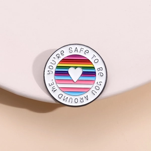 Close-up of rainbow enamel pin with white heart and You're Safe To Be You Around Me text