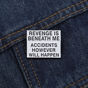 Enamel badge on blue denim fabric with text Revenge Is Beneath Me Accidents Will Happen